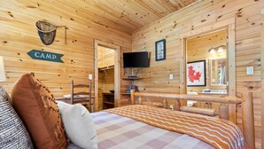 Interior de una cabaña de madera con una cama, almohadas, un televisor y un mapa en la pared.