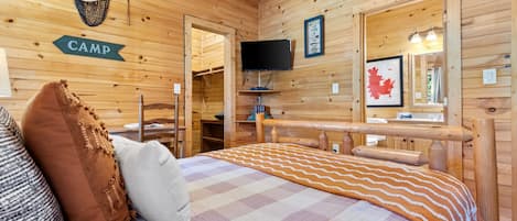 L’intérieur d’un chalet en bois, avec un lit, des oreillers, un téléviseur et une carte accrochée au mur.