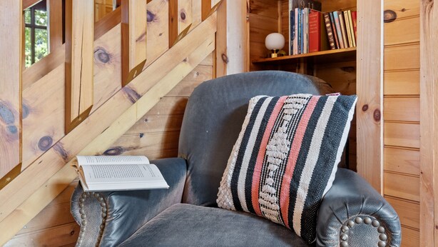 Una habitación acogedora con una escalera de madera, una estantería y un sillón de cuero con un cojín a rayas.
