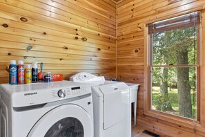 A laundry room with a Samsung washer and dryer, wooden walls, and a window with a view of trees. - Lake Views Hot Tub Fire Pit Micro Events (Morganton)