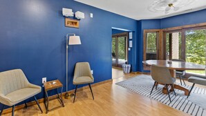 Una habitación con paredes azules, una mesa de comedor con sillas, una lámpara de pie y una ventana con vista a follaje.