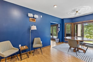Una habitación con paredes azules, una mesa de comedor con sillas, una lámpara de pie y una ventana con vista a follaje.