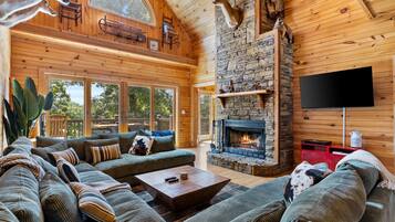 A spacious living room with a stone fireplace, a large sofa set, and a flat-screen TV mounted on the wall.
