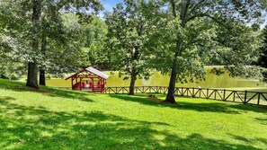 A gazebo with a roof and benches, surrounded by a fence and trees, near a body of water.
