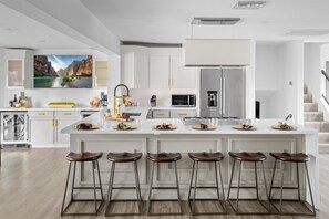 A modern kitchen with a large island, bar stools, and a refrigerator. - Casa Citrus 6BR Heated Pool Spa Modern Design (Scottsdale)
