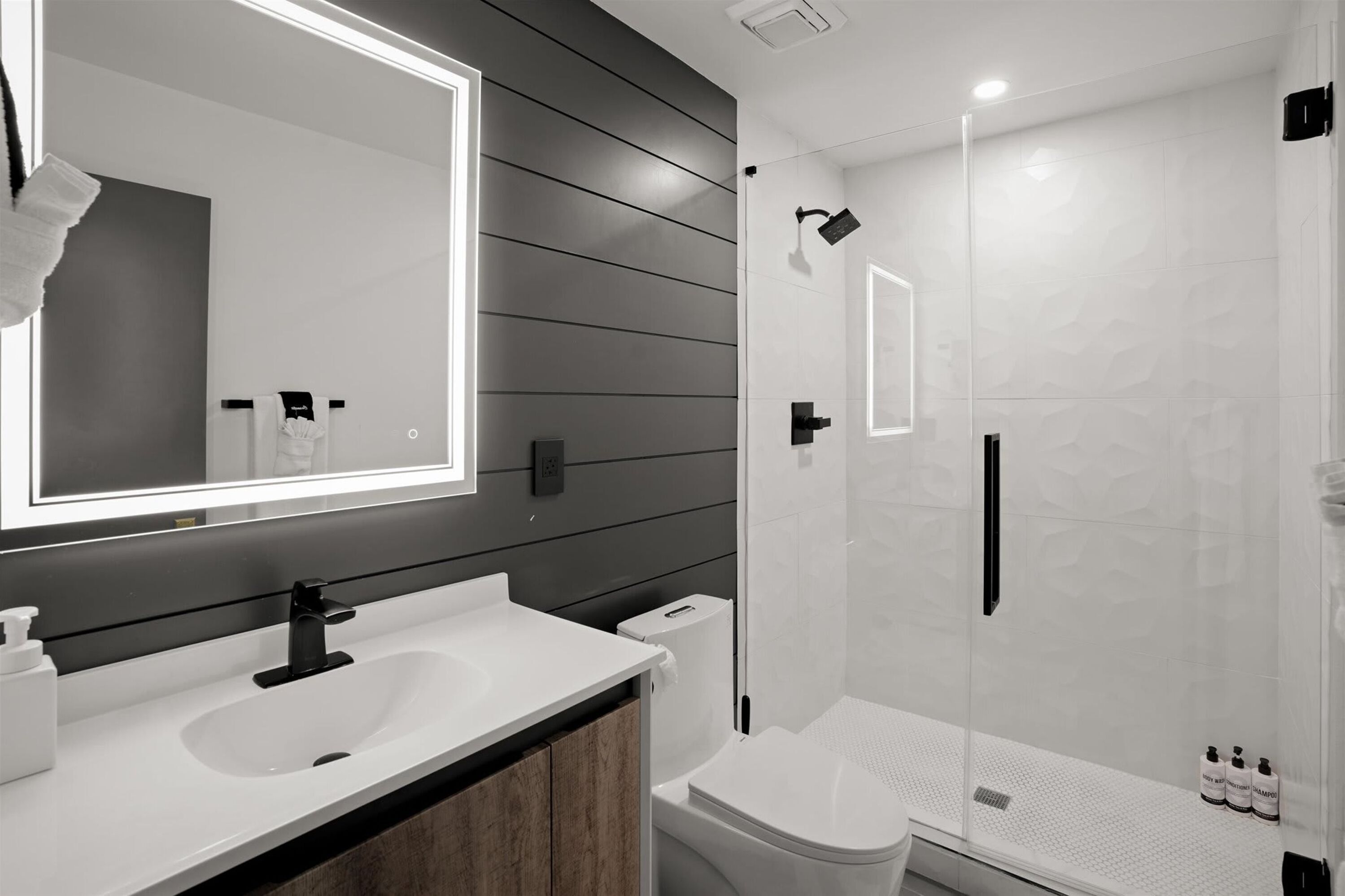 Un baño moderno con un espejo grande, un lavamanos, un inodoro y una zona de ducha.