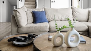 A modern living room with a round wooden coffee table, two white vases with plants, and a sofa with beige cushions and a blue pillow. - Casa Citrus 6BR Heated Pool Spa Modern Design (Scottsdale)