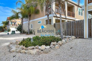 Schild für ein Strandgrundstück namens 'BEACHSIDE' mit Blick auf ein zweistöckiges Gebäude und einen Holzzaun.