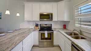 A kitchen with white cabinets, a stainless steel oven, a microwave, and a sink. - Piggy s Perch- 2 Balconies Direct Pool Access (Port Aransas)