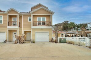 A two-story residential building with a garage, a balcony, and a fenced yard. - Piggy s Perch- 2 Balconies Direct Pool Access (Port Aransas)