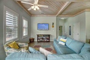 Un salon avec un ventilateur de plafond, un téléviseur, une bibliothèque et un canapé bleu.
