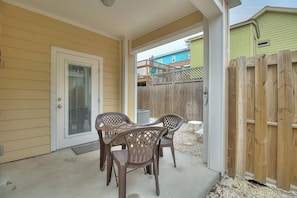 A covered patio with a table and chairs, a wooden fence, and a door with a window. - Piggy s Perch- 2 Balconies Direct Pool Access (Port Aransas)