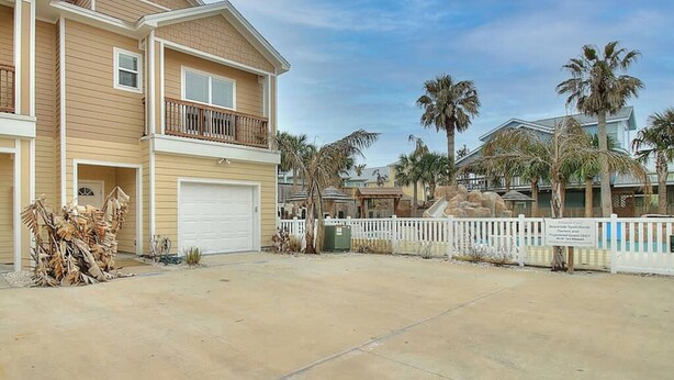 A two-story residential building with a garage, a balcony, and a fenced yard. - Piggy s Perch- 2 Balconies Direct Pool Access (Port Aransas)