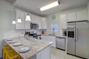 A modern kitchen with white cabinetry, a granite countertop, stainless steel appliances, and pendant lighting. - Piggy s Perch- 2 Balconies Direct Pool Access (Port Aransas)