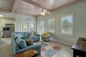 Ein geräumiges Wohnzimmer mit einem Ecksofa, einem gemusterten Teppich und einem Deckenventilator.