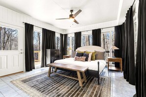 Ein Schlafzimmer mit einem Bett, einem Deckenventilator, einer Kommode, einem Nachttisch, einer Lampe und einem Fenster mit Vorhängen.
