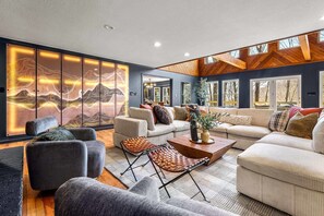 A modern living room with a large sliding door, a sofa set, a coffee table, and a view of the outdoors through large windows. - 7k sq ft Mountain Estate -the Most Epic Experience (Asheville)
