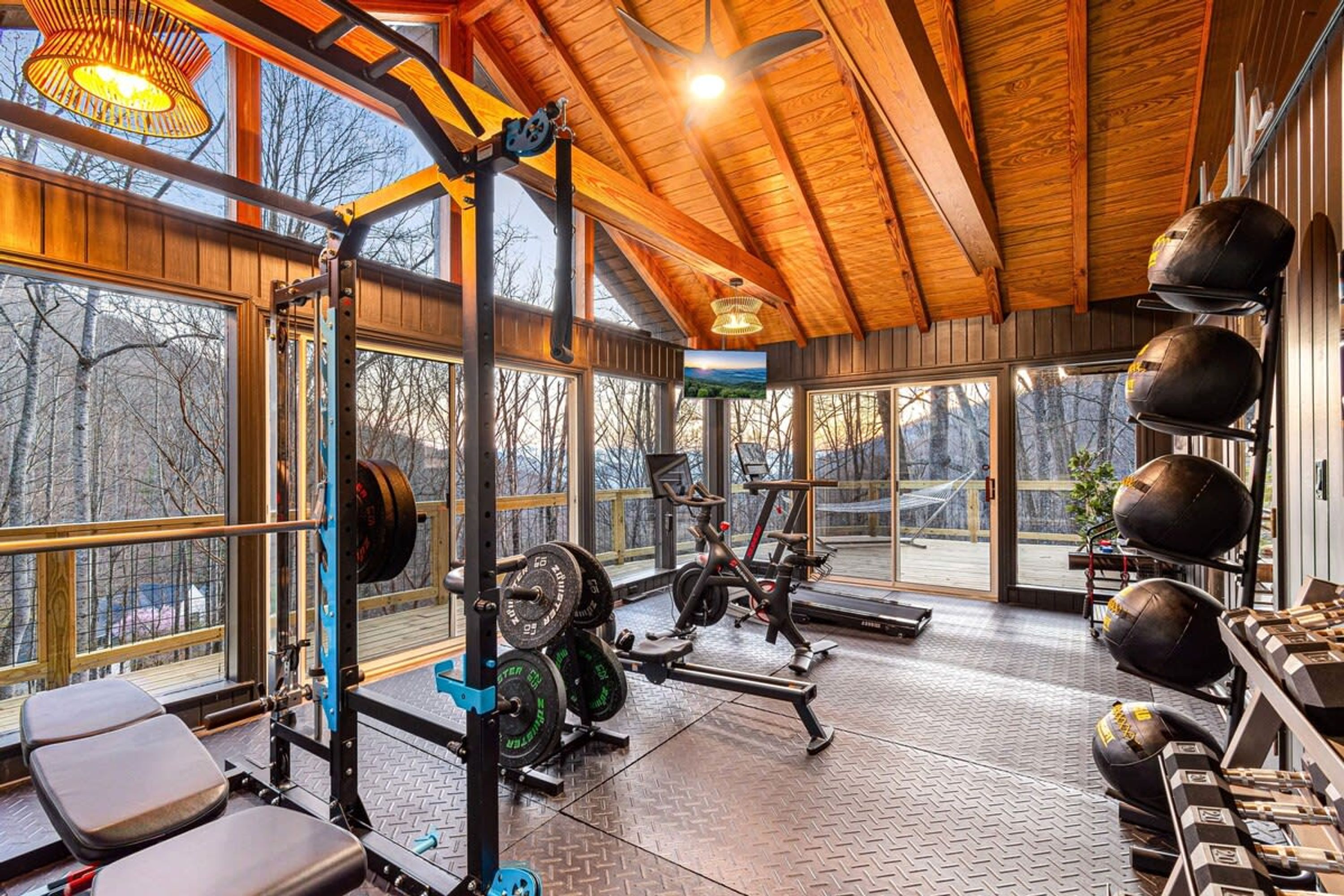 Un gimnasio con equipo de levantamiento de pesas, bicicletas estáticas y un amplio ventanal con vistas a árboles.