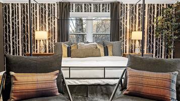 A bedroom with a bed, two armchairs, a window, and a wall with a tree pattern.