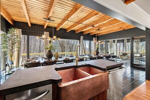 A modern kitchen with a large copper sink, wooden ceiling beams, and large windows offering views of trees. - 7k sq ft Mountain Estate -the Most Epic Experience (Asheville)