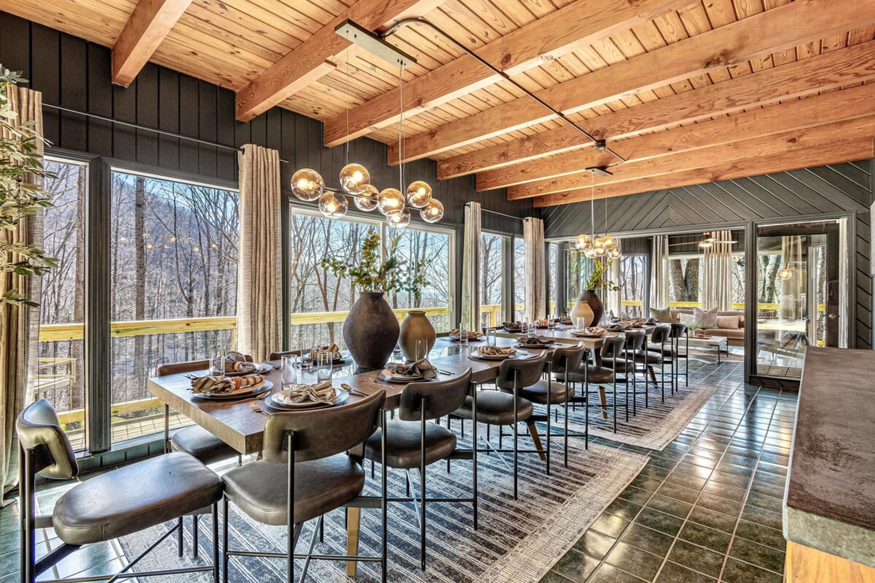 Un vaste espace dédié à la salle à manger, avec une longue table, de nombreuses chaises et de grandes fenêtres donnant sur l’extérieur.
