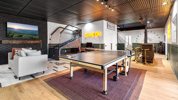 A modern indoor space with a ping pong table, a sofa, and a staircase. - 7k sq ft Mountain Estate -the Most Epic Experience (Asheville)