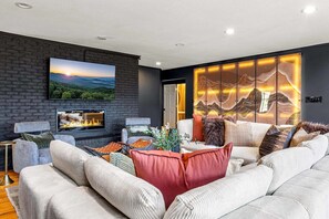 A modern living room with a fireplace, comfortable seating, and a large TV mounted on the wall. - 7k sq ft Mountain Estate -the Most Epic Experience (Asheville)