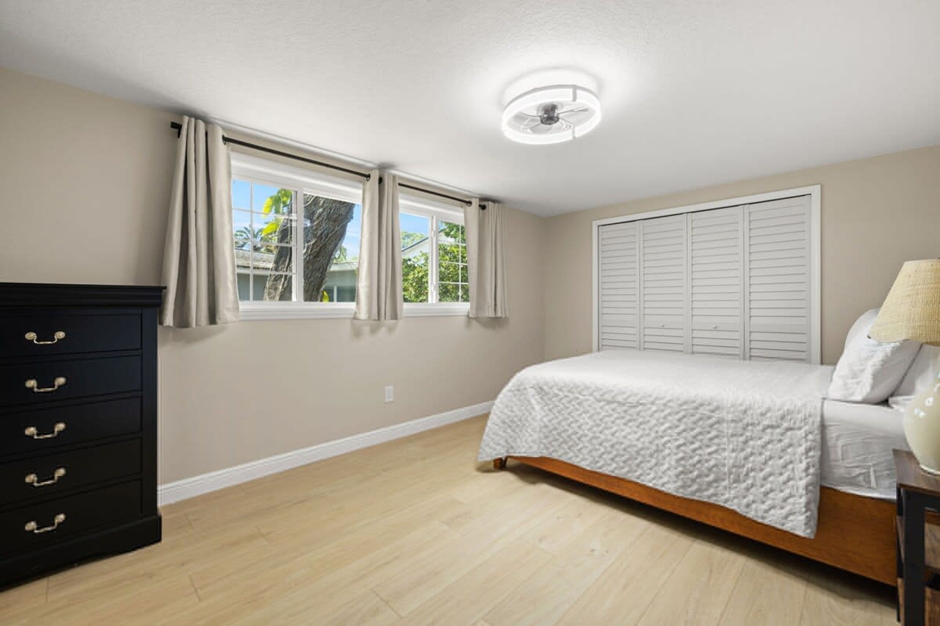 Quarto com cama, cômoda, janela e ventilador de teto.