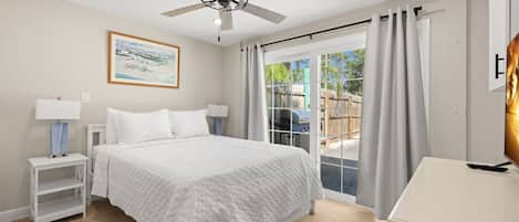 A bedroom with a bed, nightstands, a ceiling fan, a painting, and a view through a glass door.