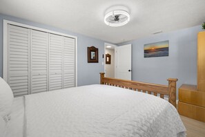 Ein Schlafzimmer mit Bett, Kleiderschrank, Spiegel, einem Bild an der Wand und Deckenventilator.