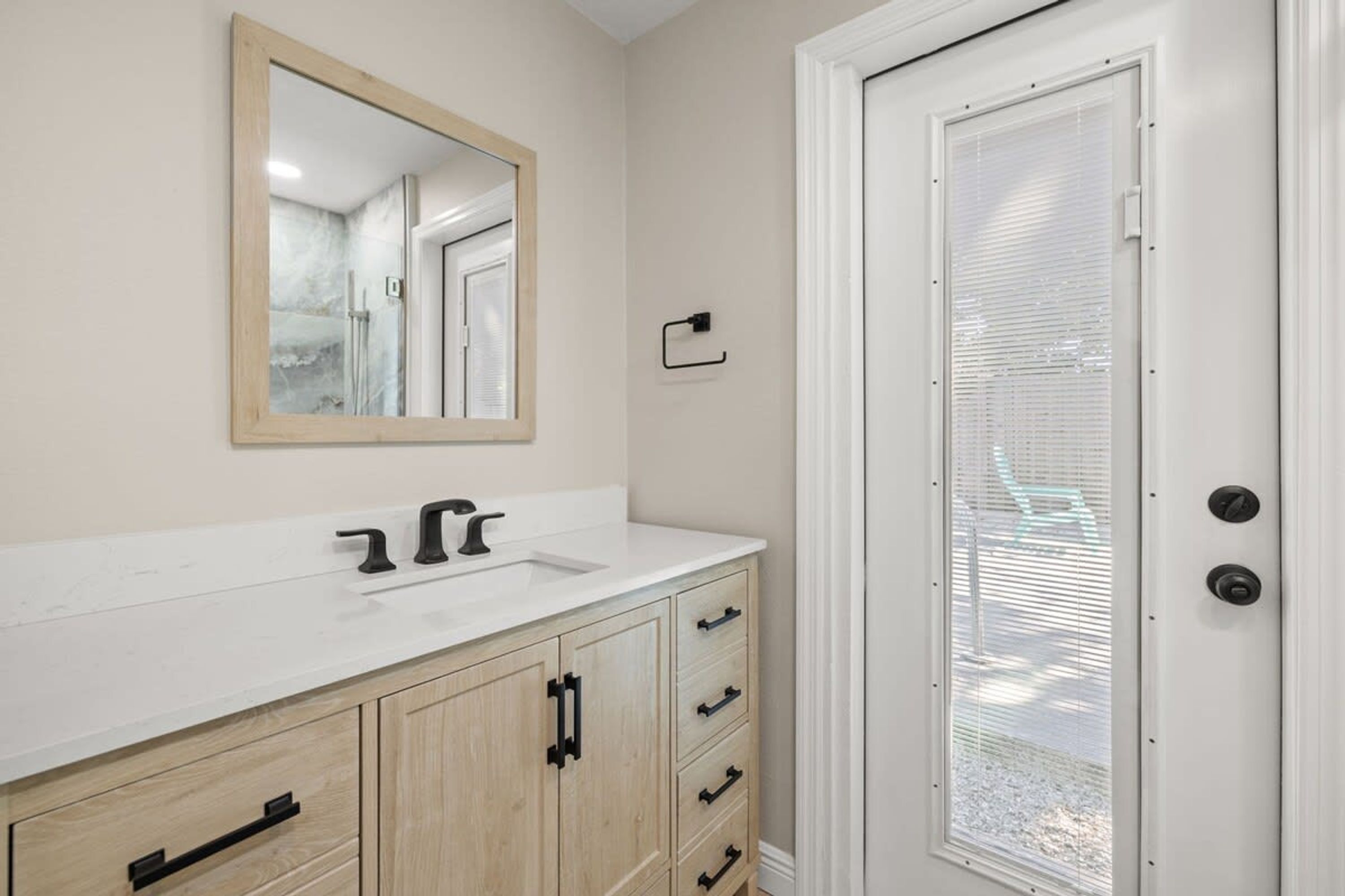 A bathroom with a white vanity, a mirror, and a door with a window.
