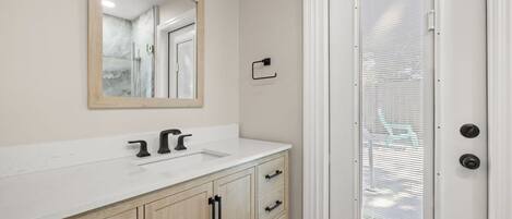 A bathroom with a white vanity, a mirror, and a door with a window.