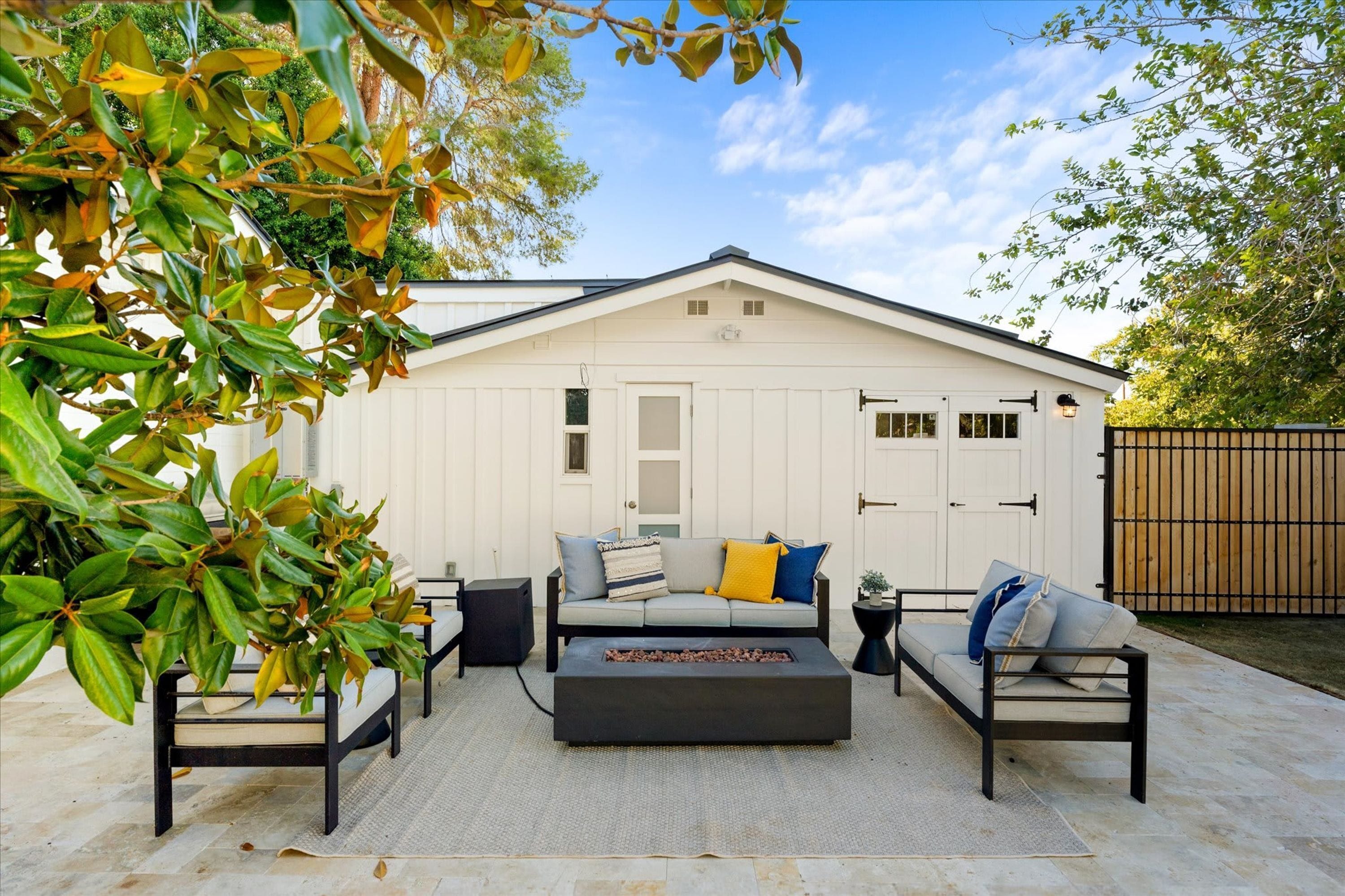 A covered patio area with a white building in the background, a sofa, two chairs, and a coffee table.