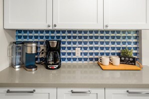 Een keuken met witte kastjes, een koffiezetapparaat, een waterkoker en een dienblad met mokken.