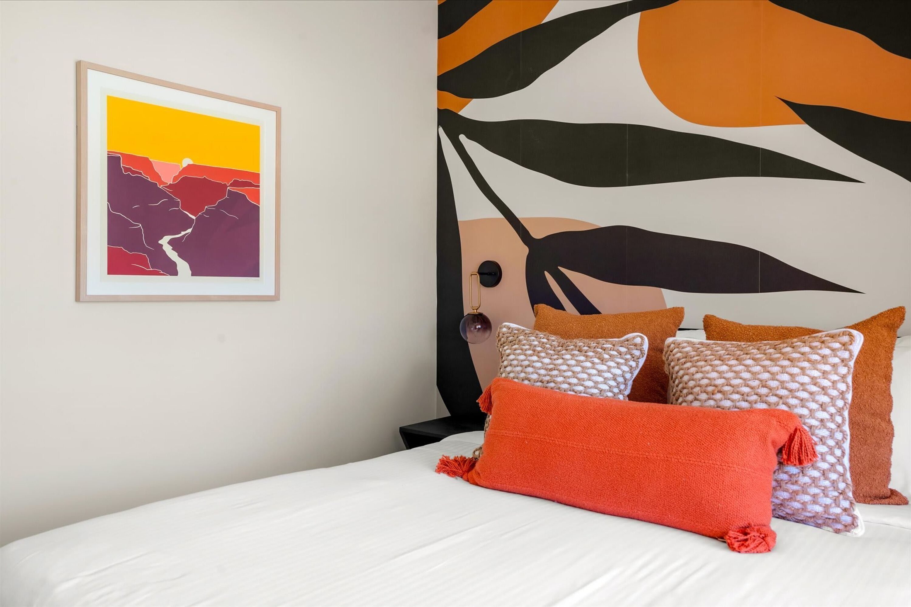 A bedroom with a bed, pillows, a framed picture, and a wall with a leaf pattern.