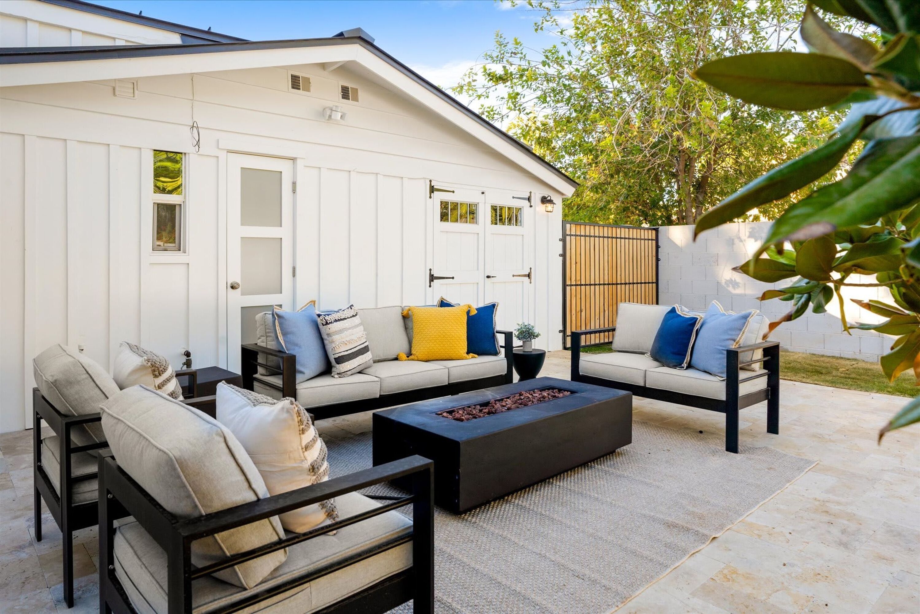 An outdoor seating area with two sofas and a coffee table, a white building in the background, and a wooden fence.
