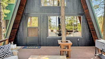 Una moderna cabaña de madera tipo A con terraza, un brasero y asientos exteriores.