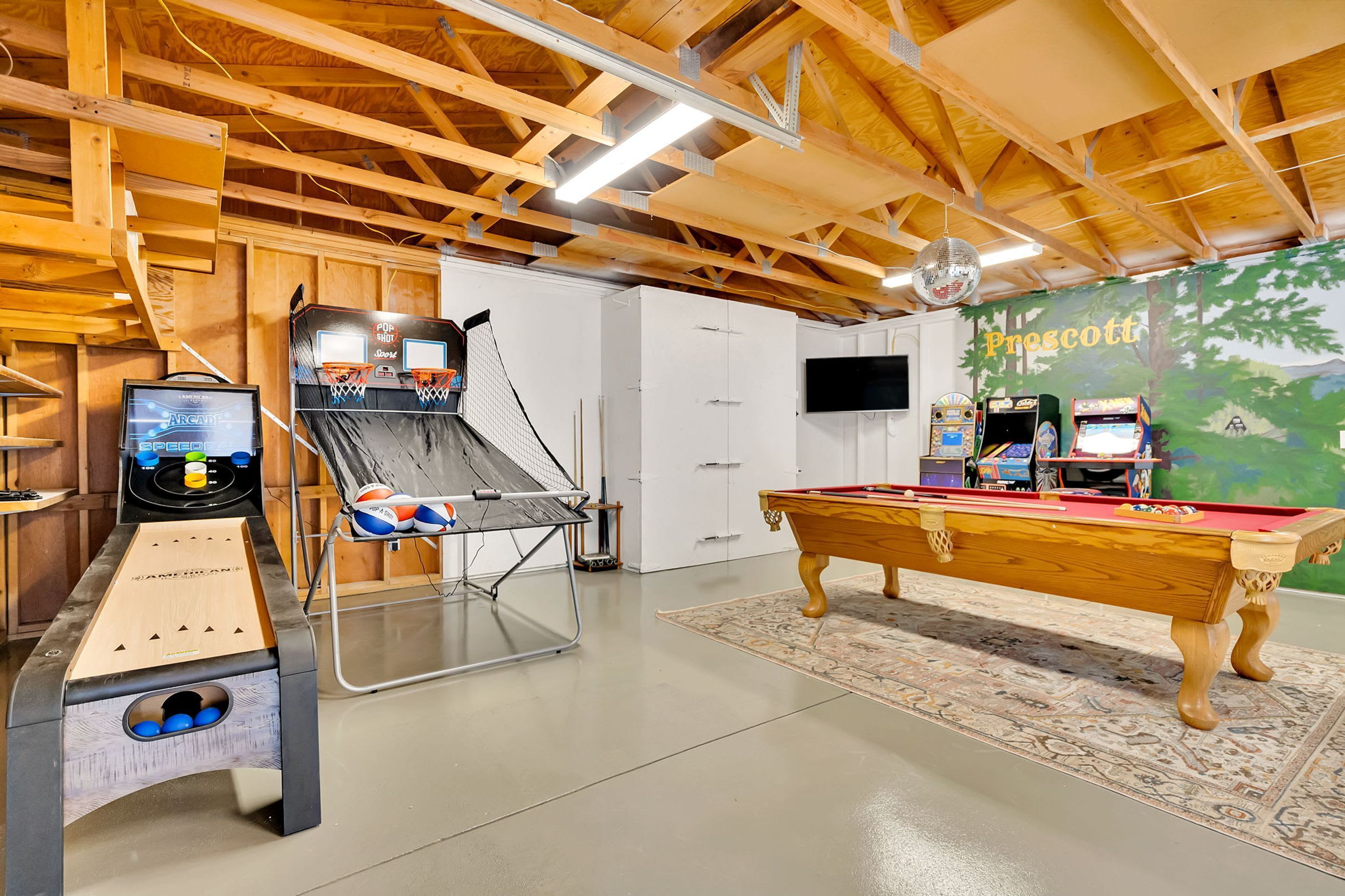 A recreational room with a pool table, arcade machines, and a basketball hoop.