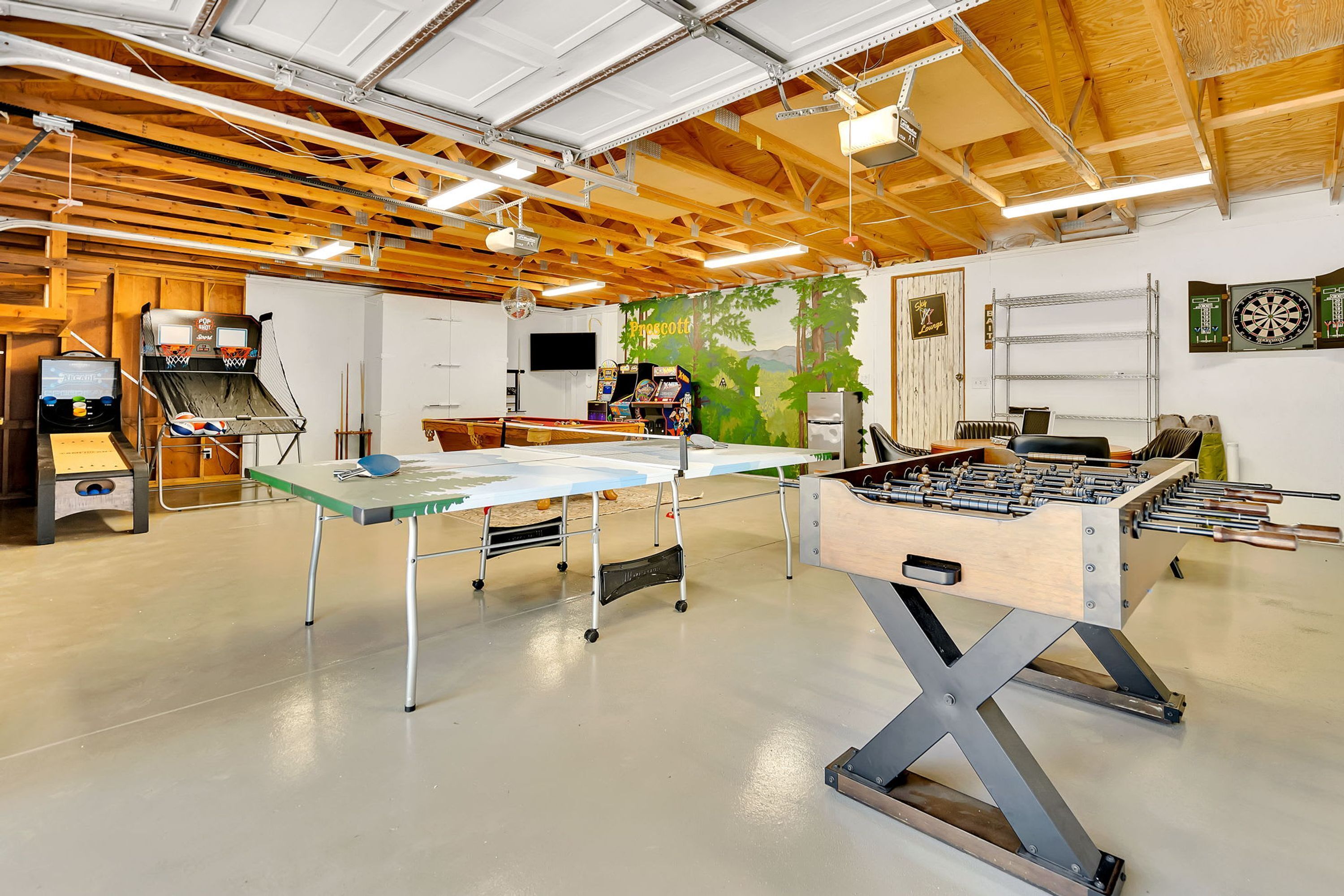 A recreational room with a foosball table, ping pong table, and a dartboard.