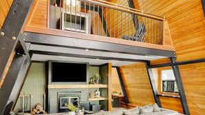 Quarto estilo loft com mezanino, piso de madeira, lareira e ventilador de teto.