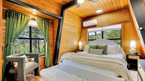 Quarto com cama, uma cadeira, ventoinha no teto e janela com cortinas.