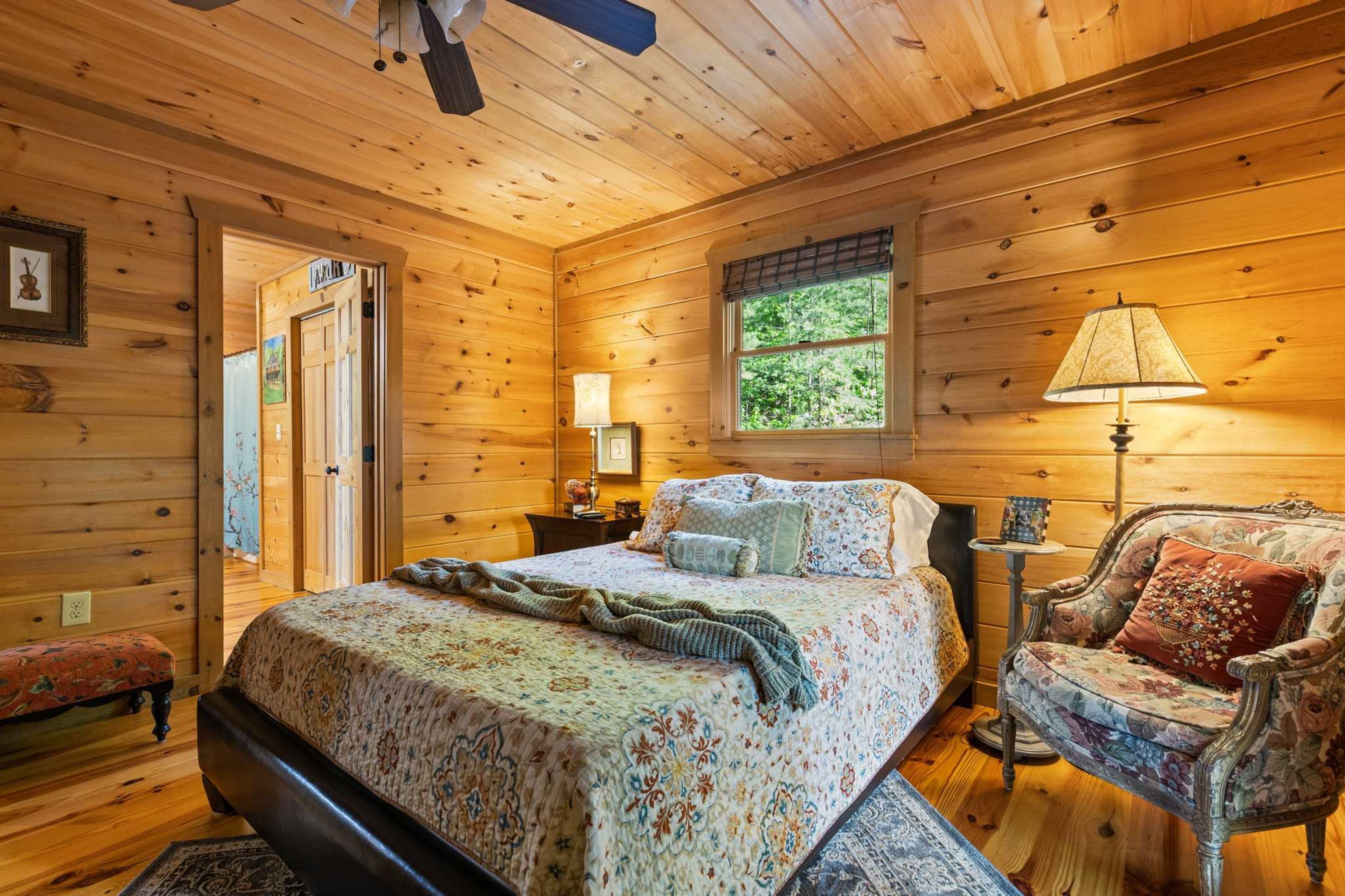 A wooden cabin bedroom with a bed, a chair, a window, and a door.
