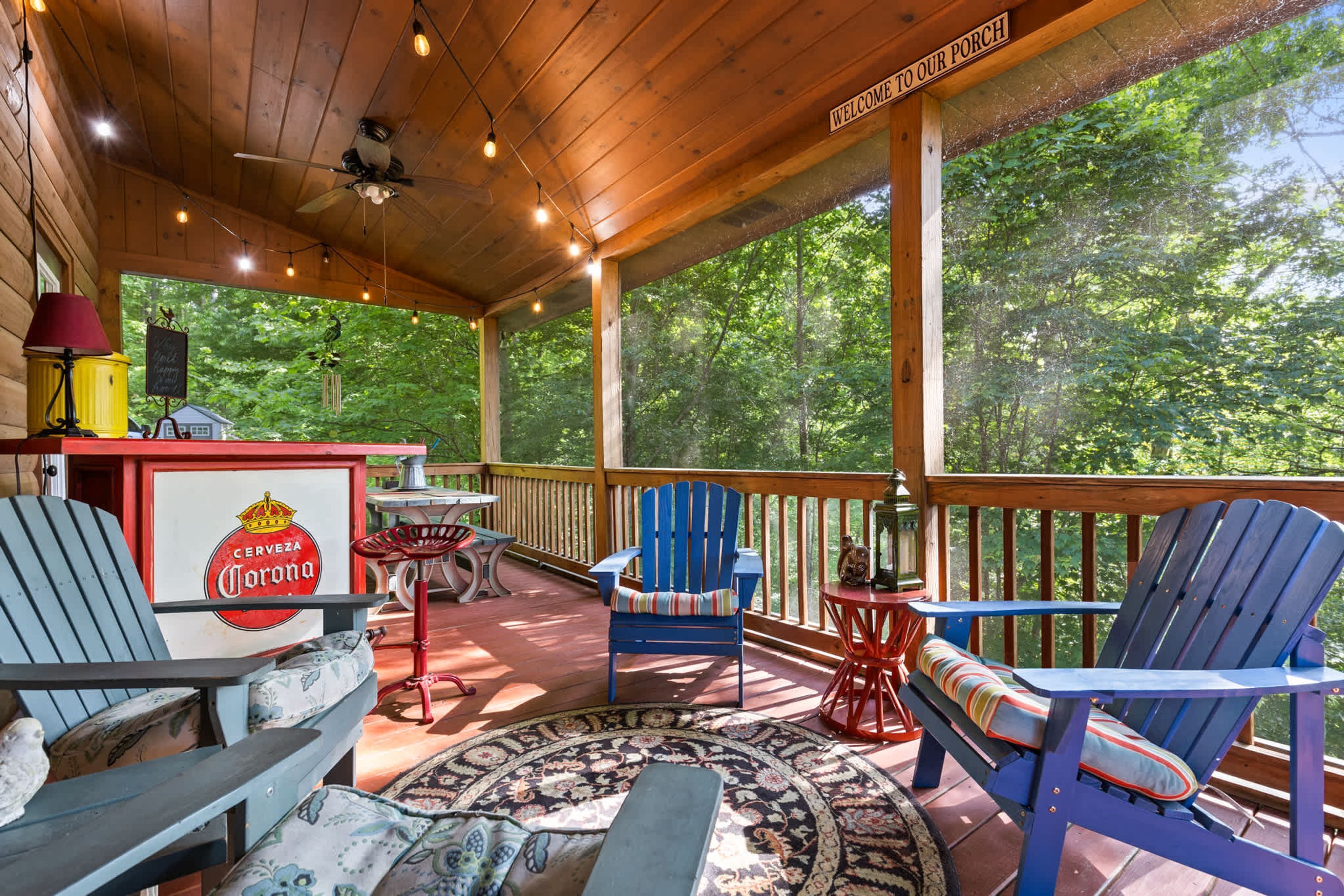 A covered outdoor area with a wooden ceiling, a sign reading 'Welcome to our porch,' and a view of a forest.