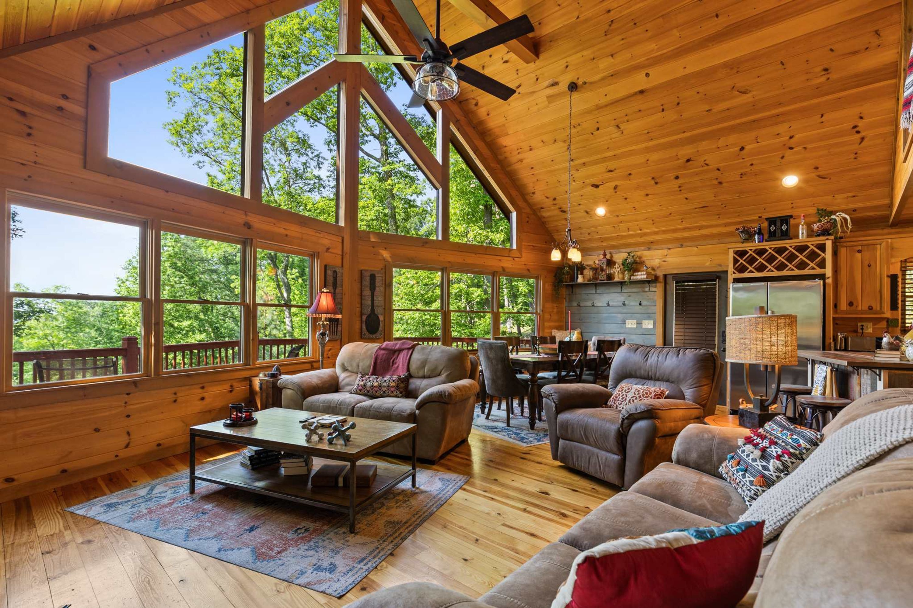 A spacious cabin interior with a high ceiling, large windows, a dining area, and a kitchen.