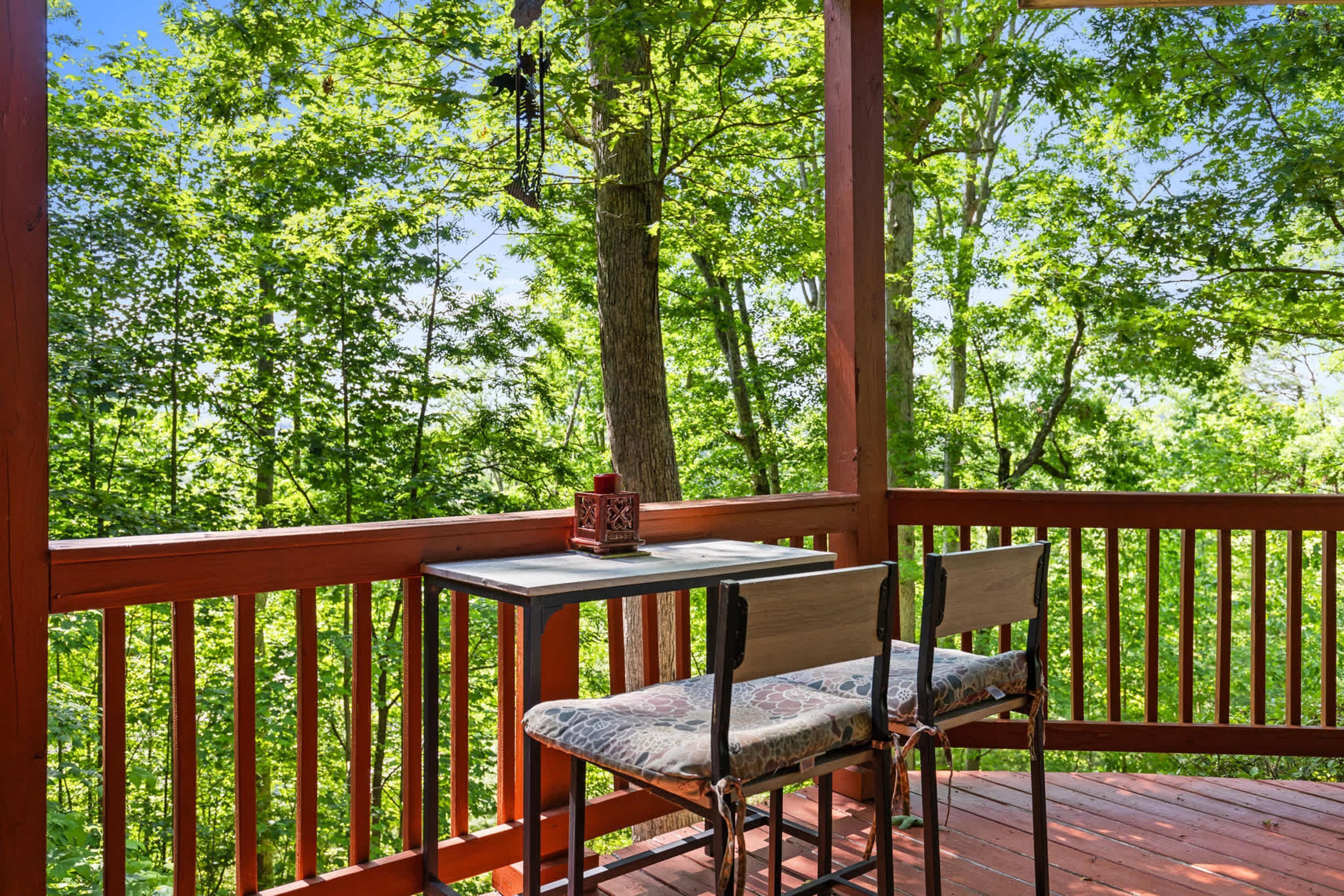 A wooden deck with a table and a chair, surrounded by a railing, overlooking a forest.