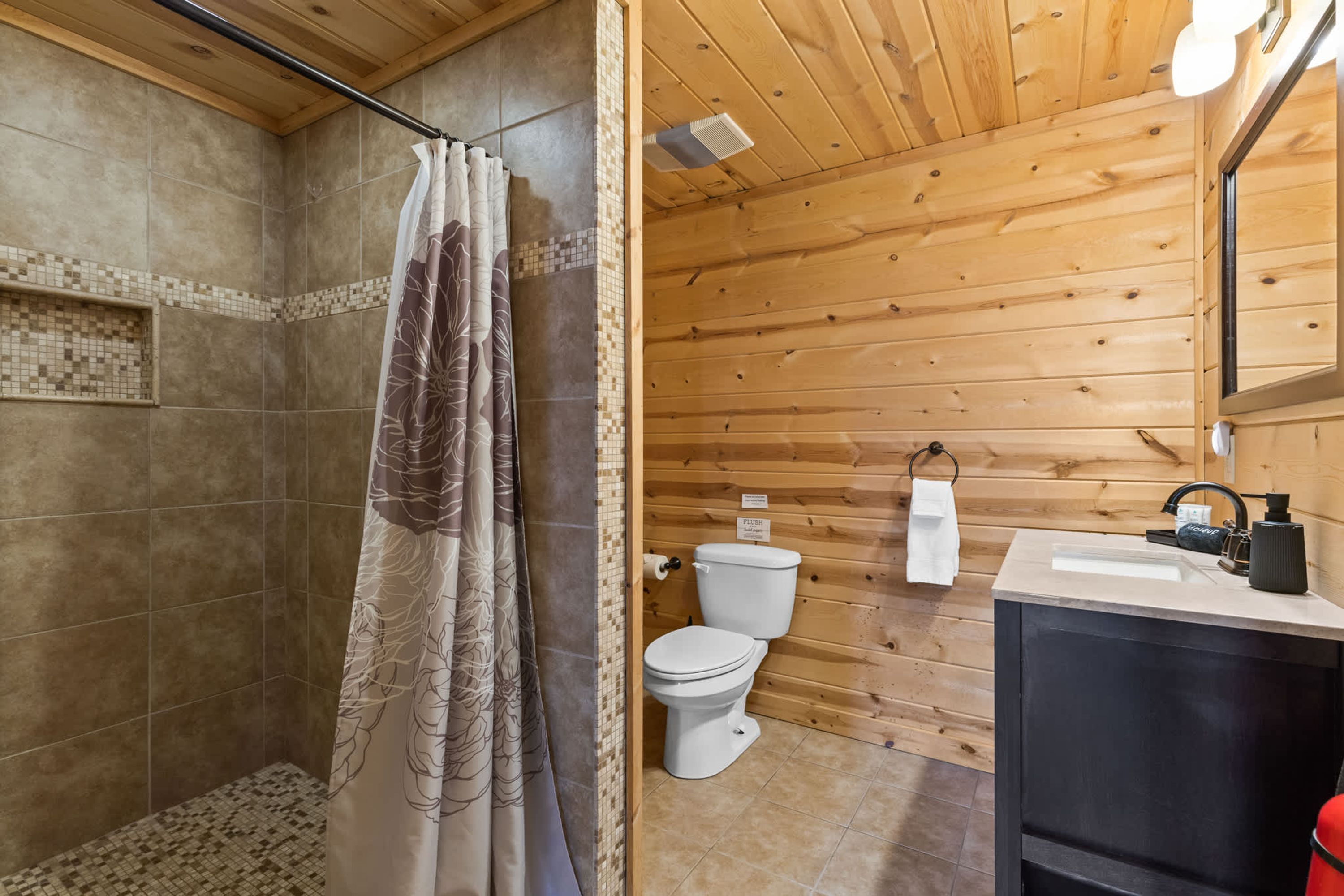 Un baño de cabaña de madera con ducha, inodoro y lavamanos.