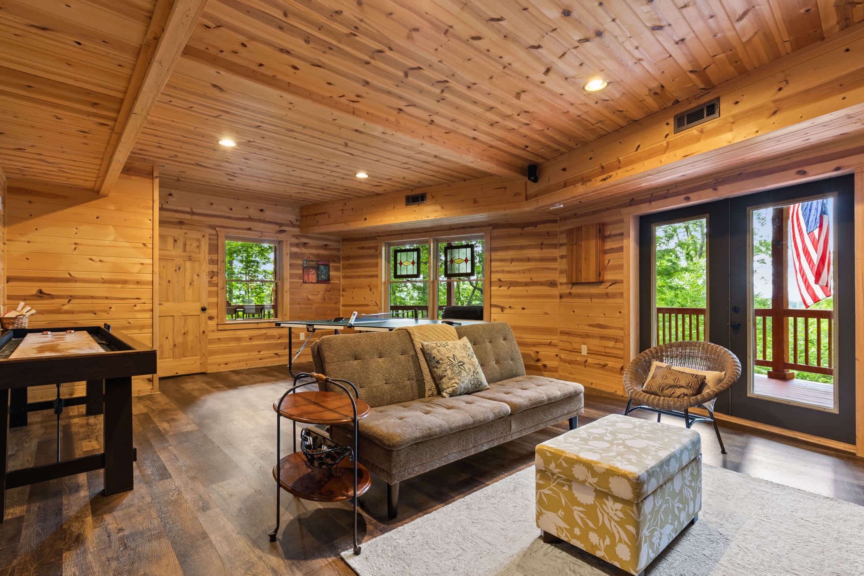 A cozy cabin interior with a sofa, ottoman, and a ping pong table.