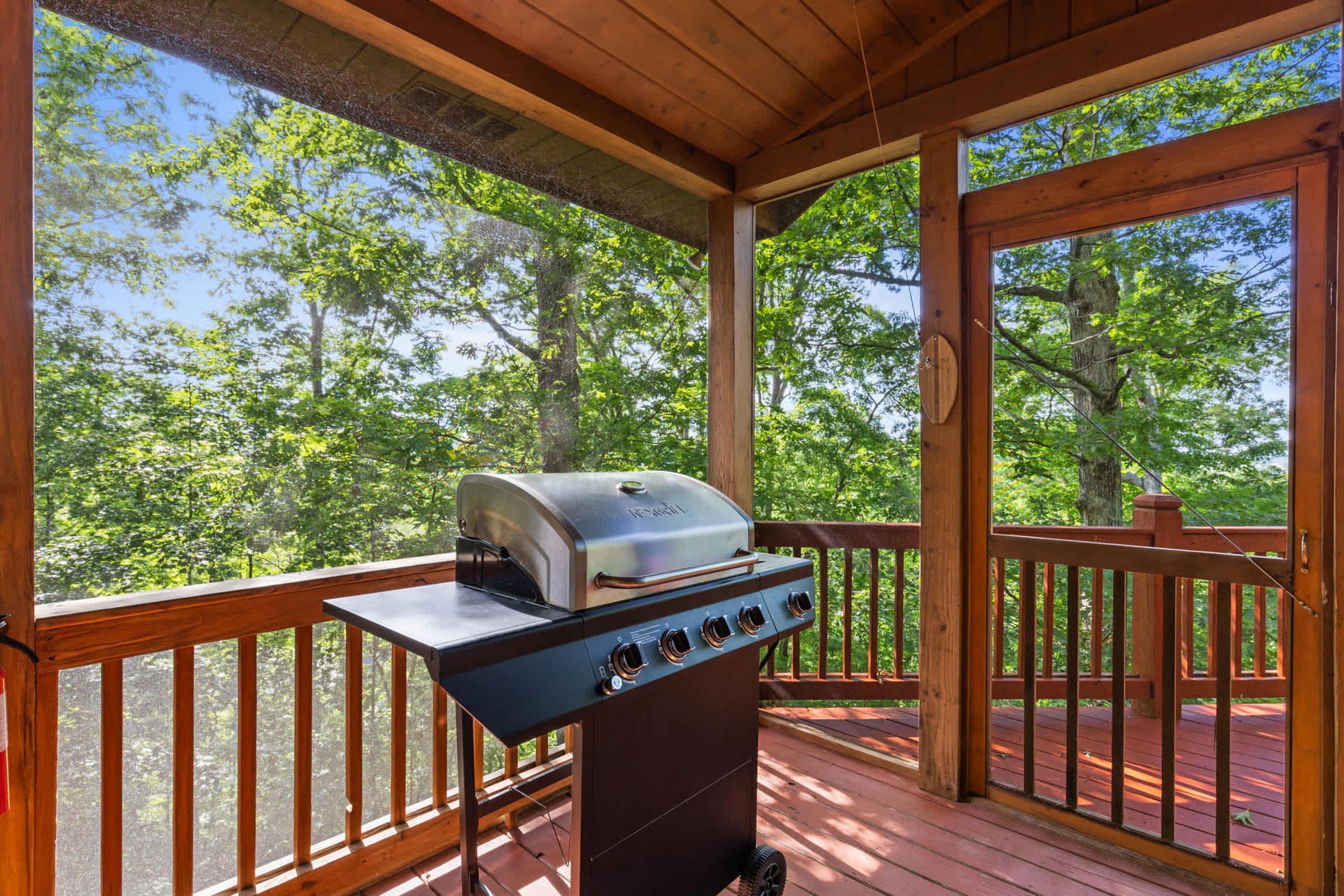 Un barbecue extérieur installé sur une terrasse en bois, avec vue sur une forêt.