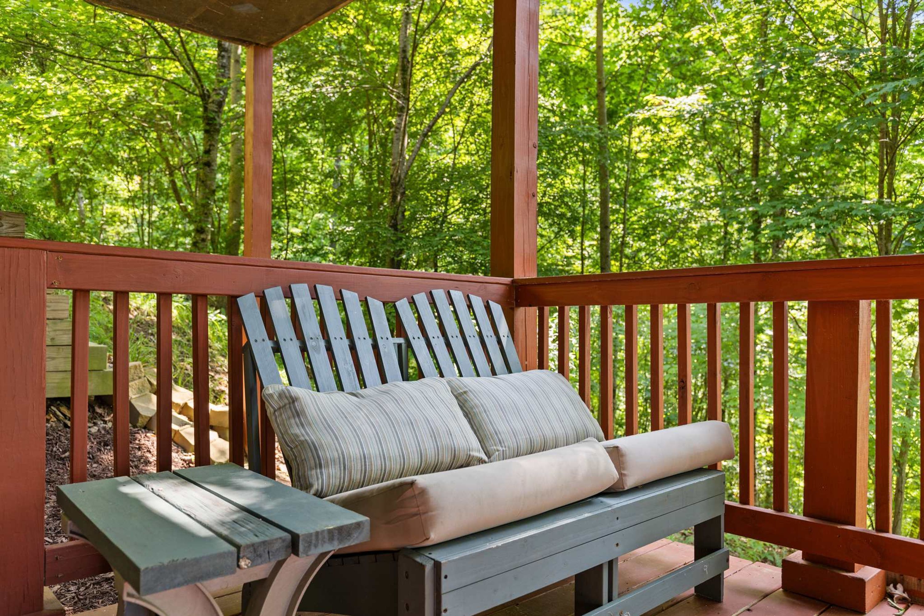 A wooden deck with a bench and a table, surrounded by trees.