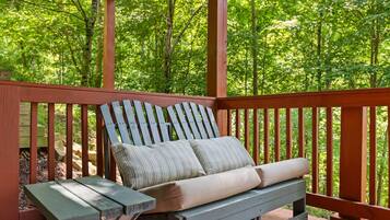 A wooden deck with a bench and a table, surrounded by trees.